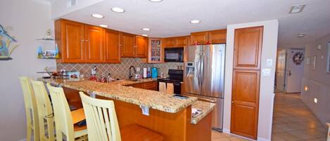 A kitchen with wooden cabinets, a stainless steel refrigerator, and a granite countertop.