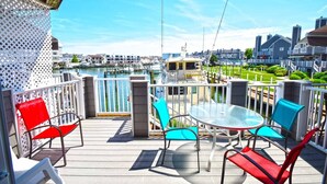 Une terrasse dotée d’une table et de chaises en verre, offrant une vue sur une marina avec des bateaux et des bâtiments.