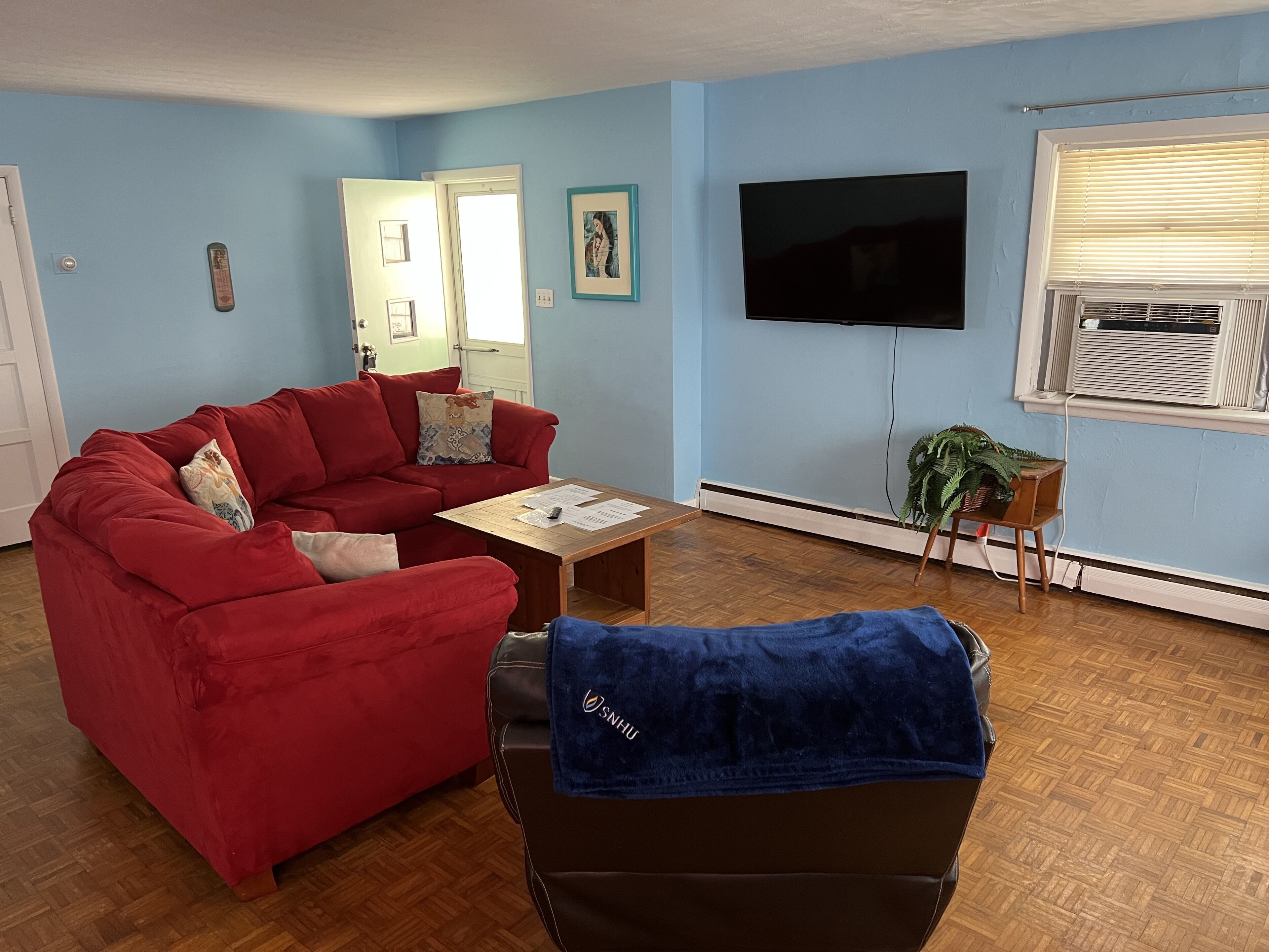 A living room with a red sofa, a wooden coffee table, a TV, and a window with blinds.