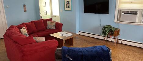 A living room with a red sofa, a wooden coffee table, a TV, and a window with blinds.