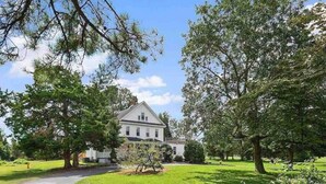 A large, white building with a symmetrical facade, surrounded by lush green trees and a well-maintained lawn.