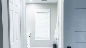 A hallway with white doors, a radiator, a window with blinds, and a black trash can.