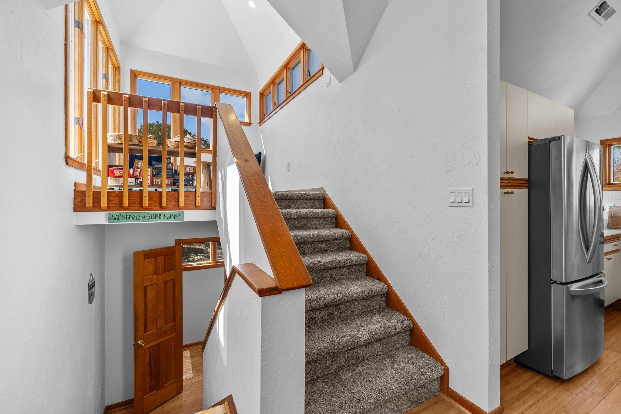 Un escalier avec des rampes en bois et des marches recouvertes de moquette, menant à une mezzanine offrant une vue sur l’extérieur.