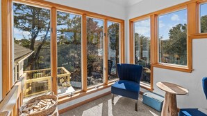 Ein Zimmer mit großen Fenstern, einem blauen Sessel, einem Holztisch und einem Korbwannenkorb.