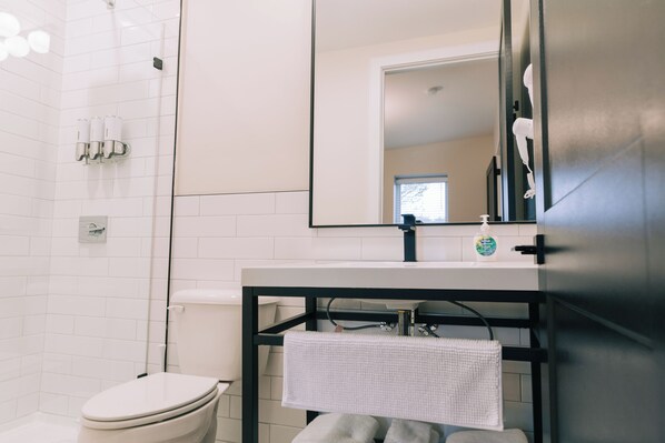 Un baño moderno con inodoro blanco, tocador con lavamanos negro y un espejo grande.