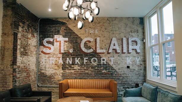 A room with a brick wall, a large sign reading "The St. Clair Hotel," and a mix of seating including a sofa and a chair. - The St. Clair (Frankfort)