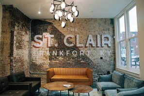 Ein Zimmer mit Backsteinwand, einem großen Schild mit der Aufschrift "The St. Clair Hotel" und einer Mischung an Sitzgelegenheiten, darunter ein Sofa und ein Sessel.