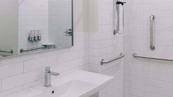 Ein modernes Badezimmer mit Waschbecken, großem Spiegel und Duschkabine mit Haltegriffen.