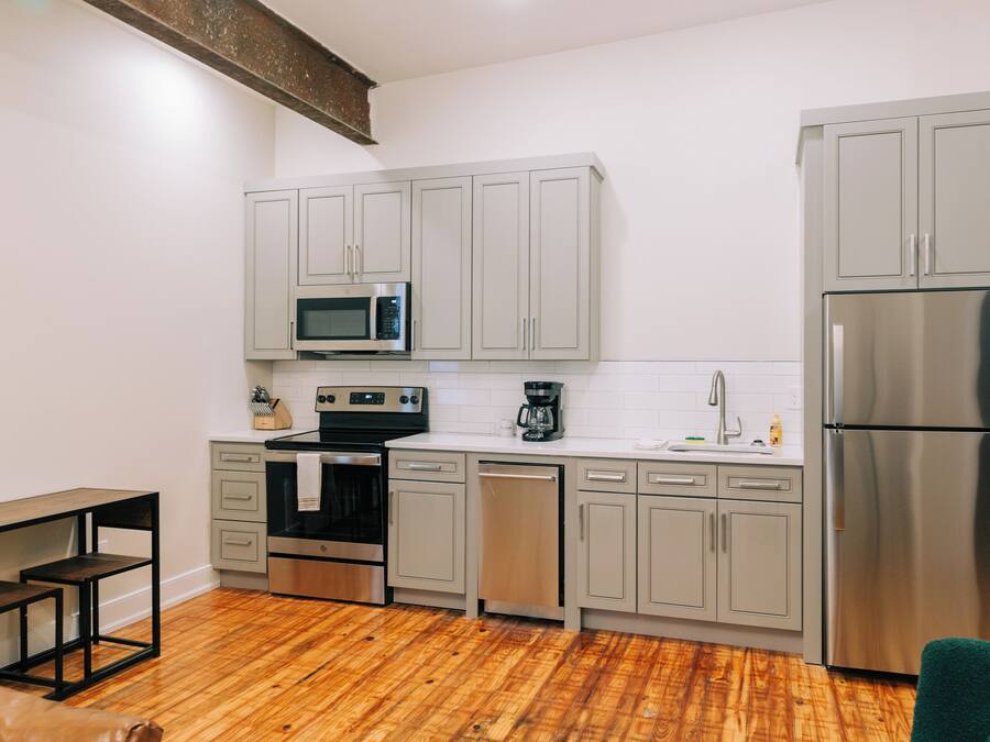 A modern kitchen with grey cabinets, stainless steel appliances, and a wooden floor.