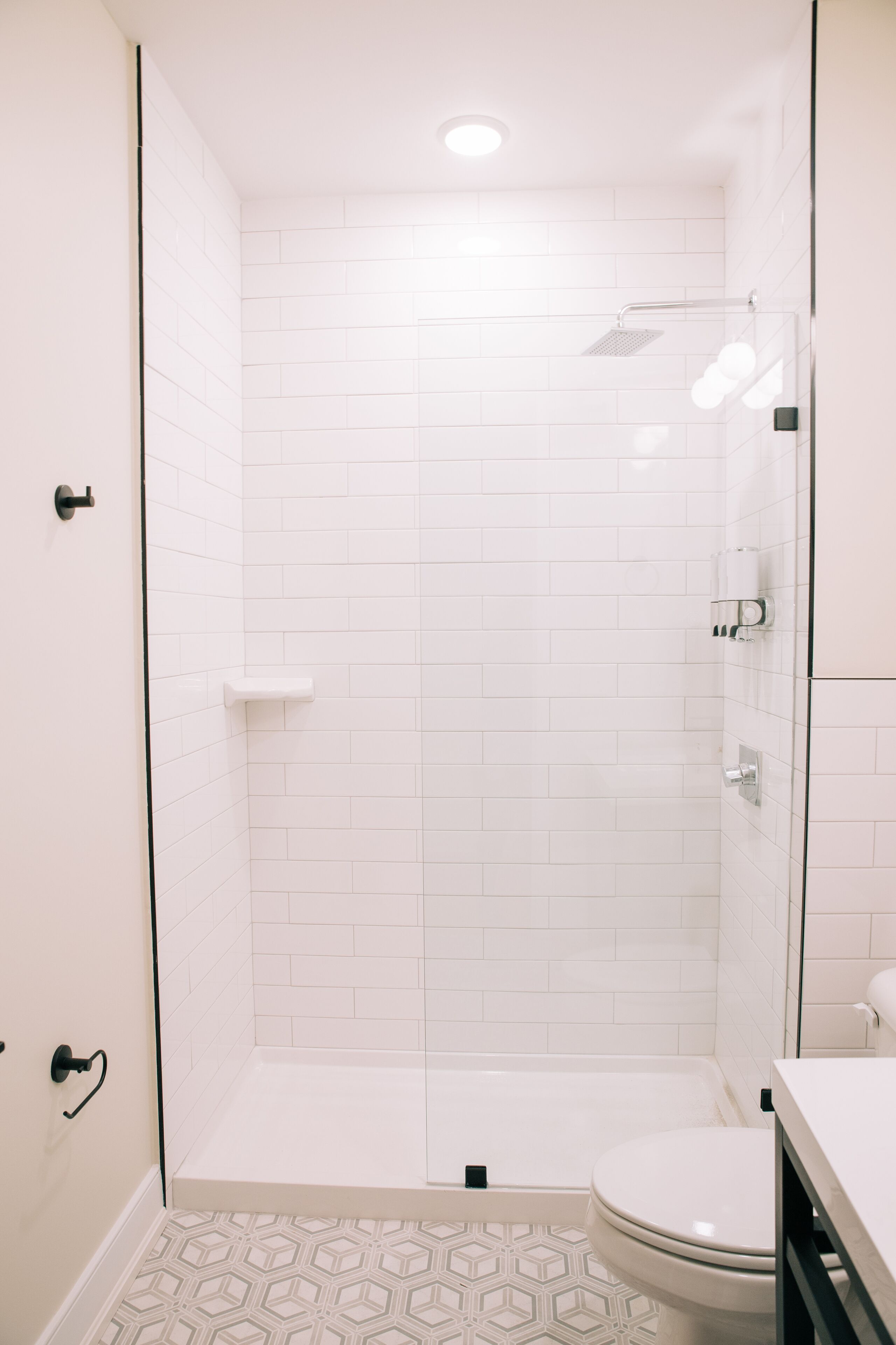 Moderni kylpyhuone, jossa on valkoiset laatat, suihku ja wc.