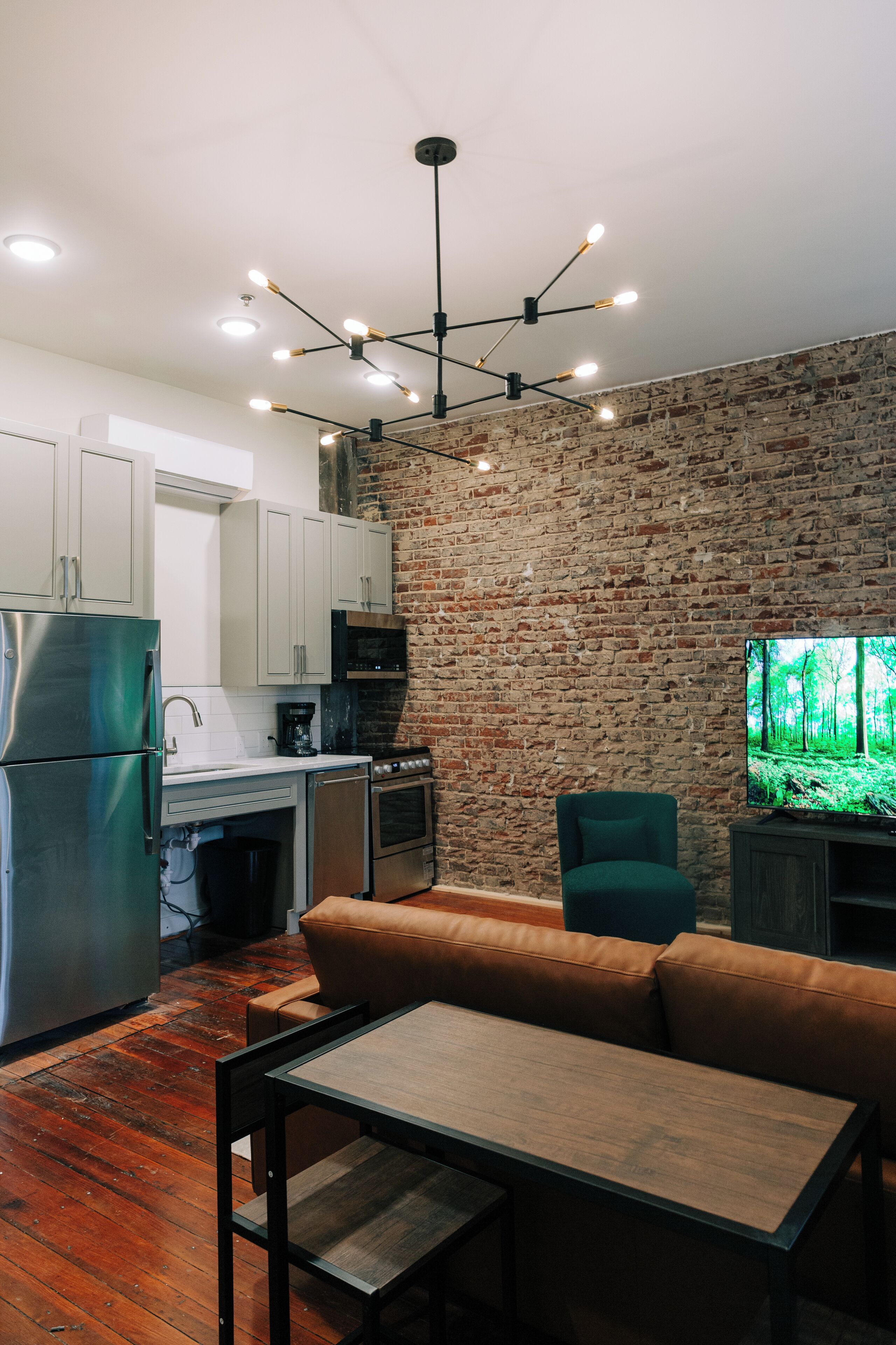 A modern kitchen with a brick wall, stainless steel appliances, and a dining area with a bench and table.