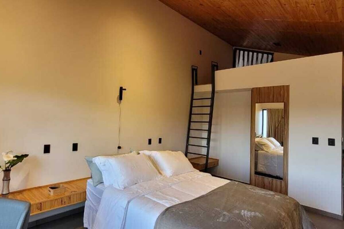 Un dormitorio moderno con cama, escritorio y silla. Hay una escalera que lleva a un nivel superior.