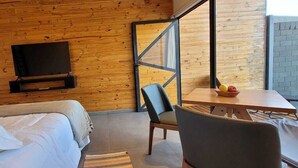Ein Hotelzimmer mit einer Holzwand, einem Bett, einem an der Wand befestigten Fernseher, einem Tisch mit einer Obstschale und einem Stuhl.