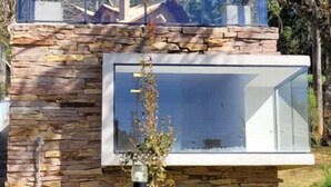Ein modernes Haus mit Naturstein-Fassade, einem Glas-Obergeschoss und einem gepflegten Rasen.