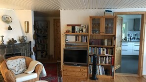 A cozy living room with a fireplace, a bookshelf, a television, and a dining area visible through an open doorway.