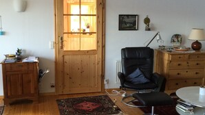 A cozy living room with a wooden door, a black leather chair, a small table with a lamp, and a wooden cabinet.