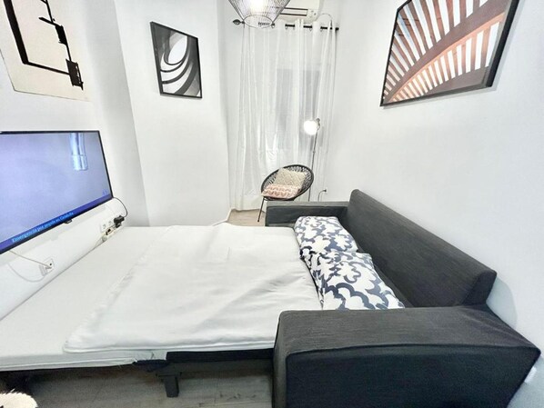 A bedroom with a bed, a chair, a desk, and a TV.