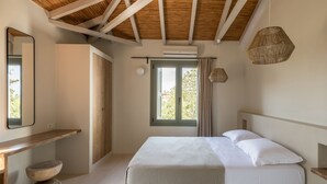 A bedroom with a wooden ceiling, a bed with white linens, a wooden nightstand, a round stool, a window with curtains, and a hanging light fixture. - Dream villa (Vasilitsi)
