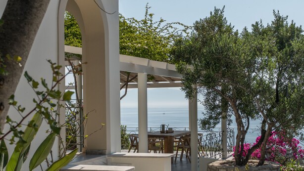 An outdoor patio with a table and chairs, surrounded by plants and a view of the sea. - Dream villa (Vasilitsi)