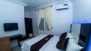 Quarto de hotel com cama, escrivaninha, cadeira, televisão e ar condicionado.