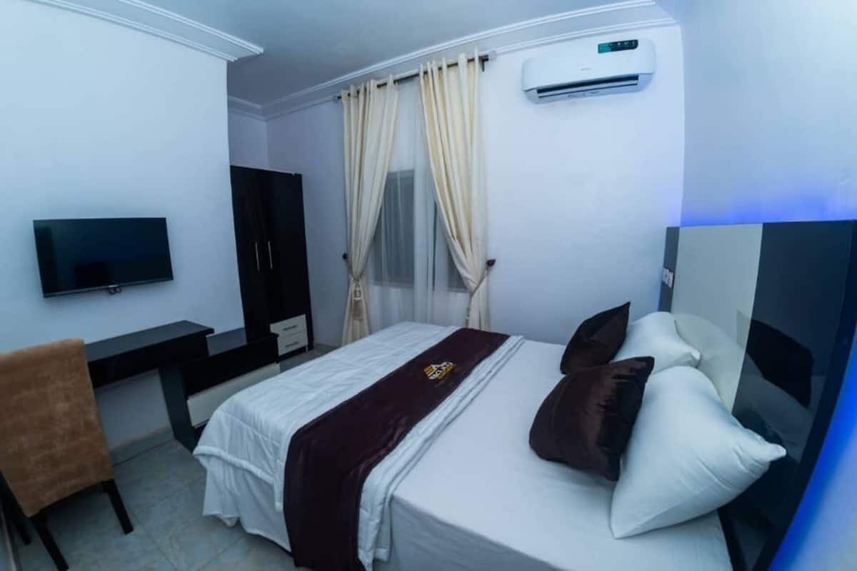Ein Hotelzimmer mit Bett, Schreibtisch, Stuhl, Fernseher und Klimaanlage.