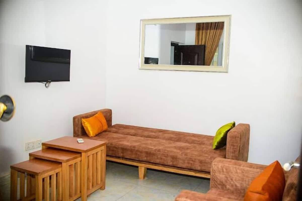 Ein Wohnzimmer mit braunem Sofa, zwei Holznachttischen, einem Flachbildfernseher und einem Spiegel an der Wand.