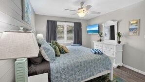 A bedroom with a bed, a ceiling fan, a dresser, a TV, and a window with curtains. - VH 206C (Siesta Key)