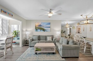 A modern living room with a grey sofa set, a coffee table, a dining area with white chairs, and a ceiling fan. - VH 206C (Siesta Key)