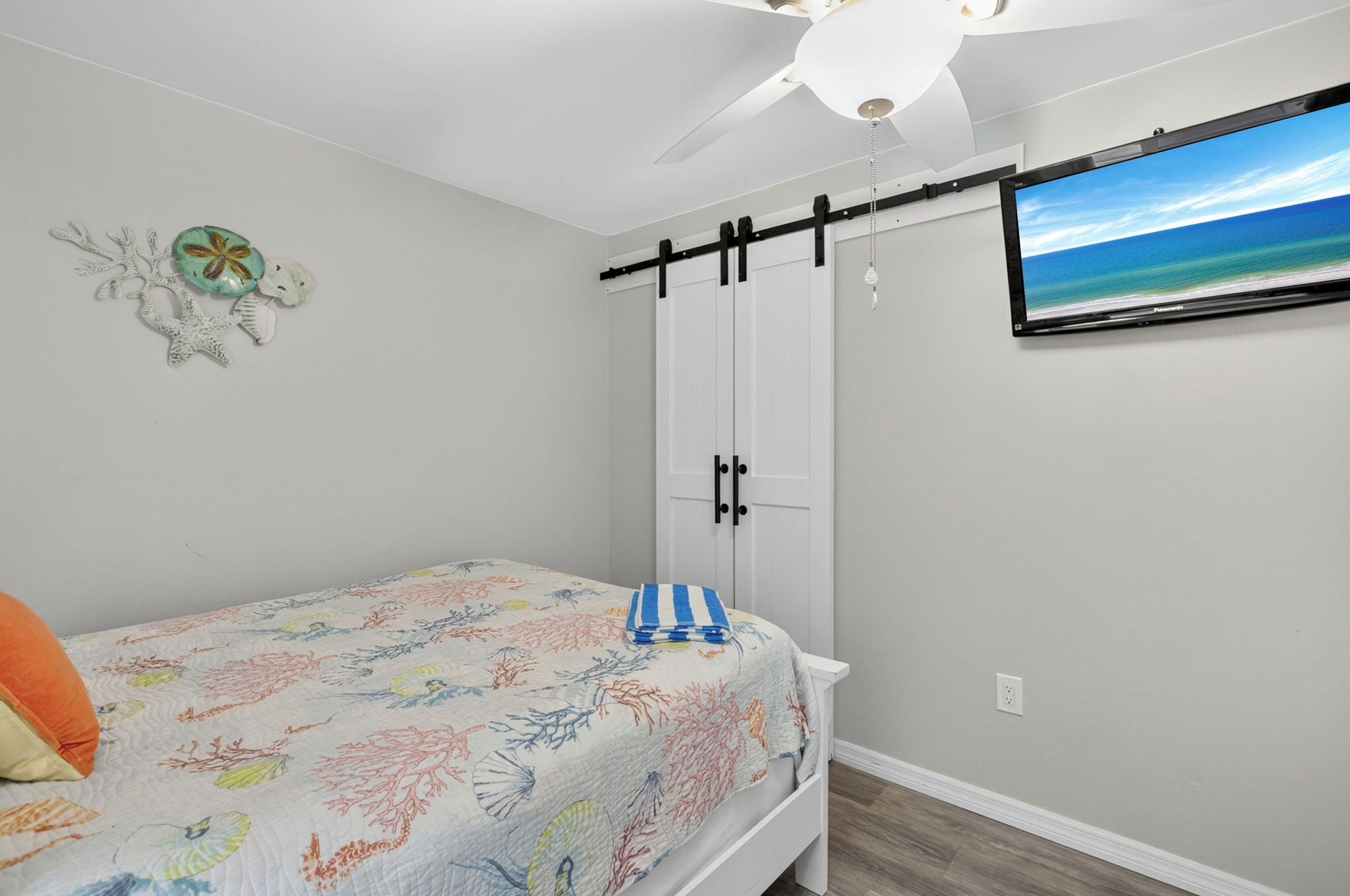 A bedroom with a bed, a ceiling fan, a wall-mounted TV, and a decorative wall piece.