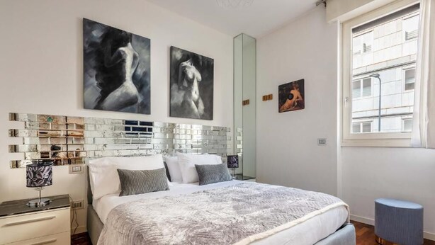 Een moderne slaapkamer met een groot bed, een nachtkastje, een spiegel en kunstwerken aan de wanden.