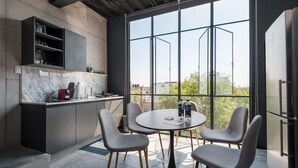 A modern kitchen with a large window, a dining table with chairs, and a refrigerator.