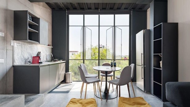 A modern kitchen with a dining area, large windows, and a view of greenery.