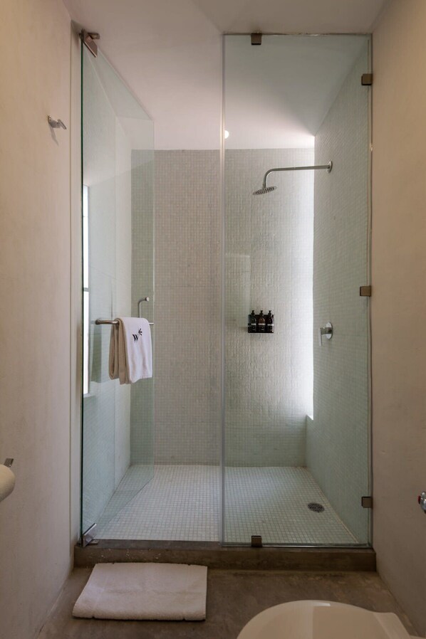 A glass-enclosed shower with a handheld showerhead, a glass door, and a small shelf with toiletries.