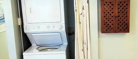 A compact laundry room with a washing machine and dryer, a wooden cabinet above, and a curtain.