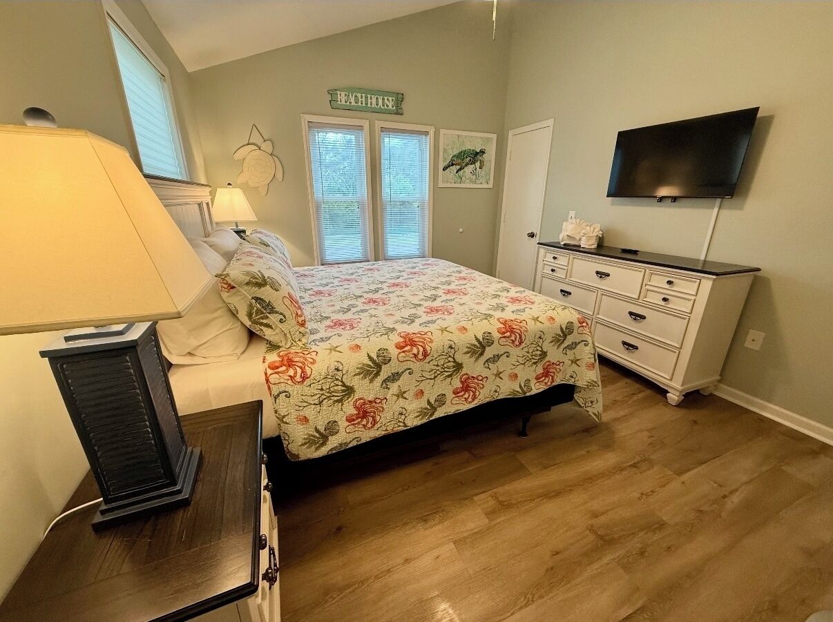 A bedroom with a bed, a dresser, a TV, and a window with blinds.