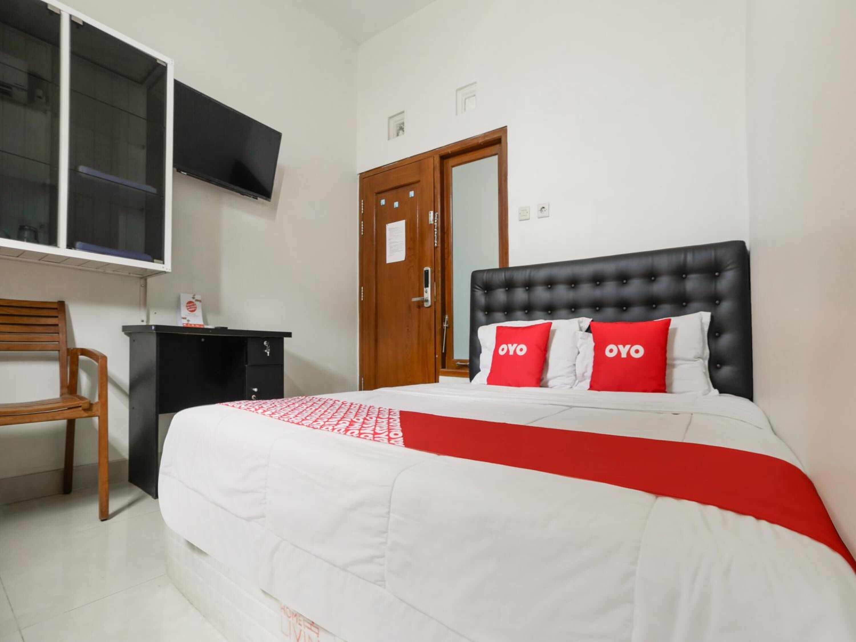 Une chambre à coucher avec un lit, une chaise en bois, un bureau, une télévision et une porte.