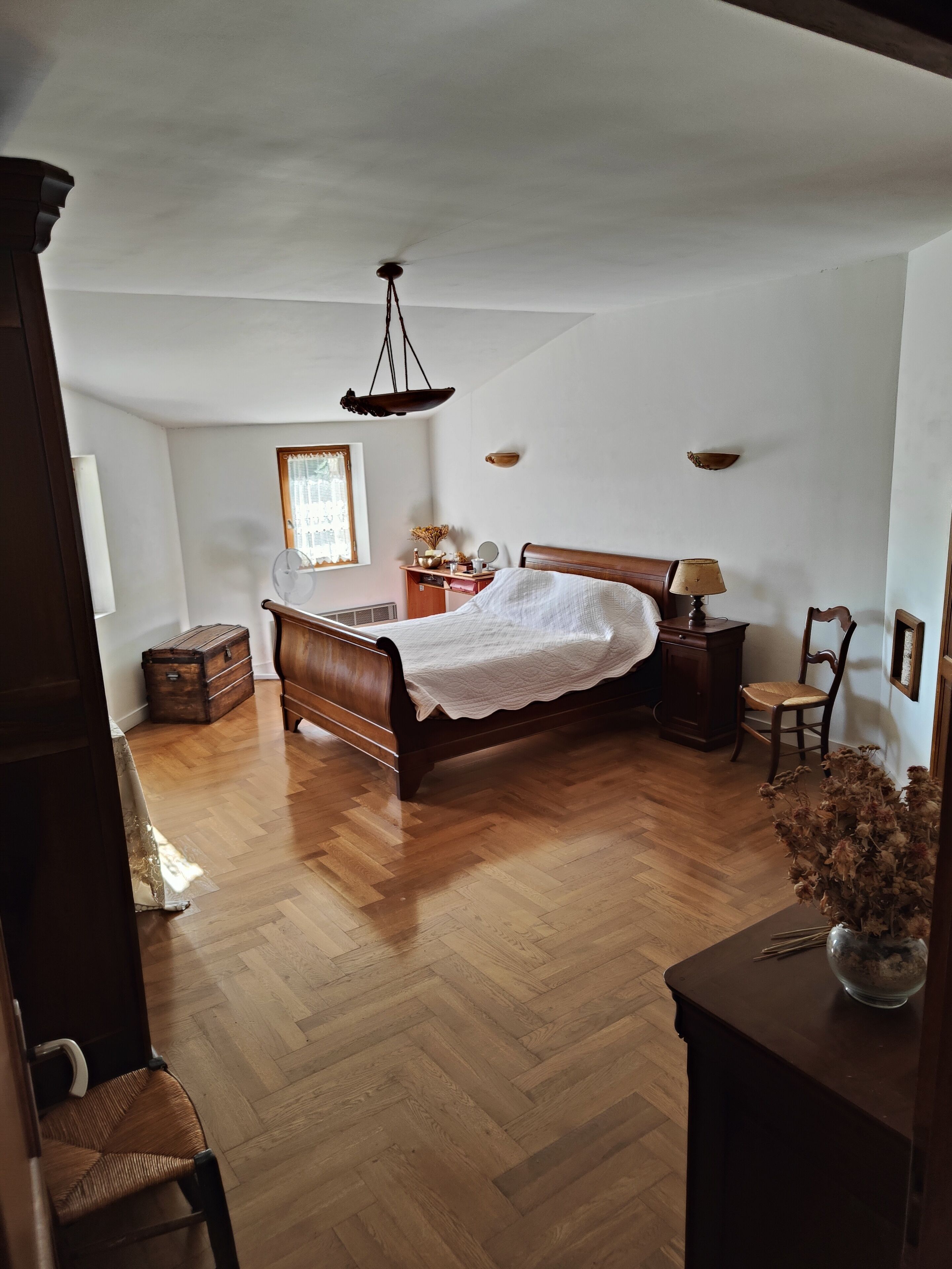 A bedroom with a wooden bed, a dresser, a chair, and a small table with a lamp.