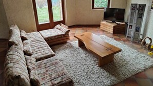 Una sala de estar con un sofá, una mesa de centro de madera, un televisor y vistas al exterior a través de amplias ventanas.