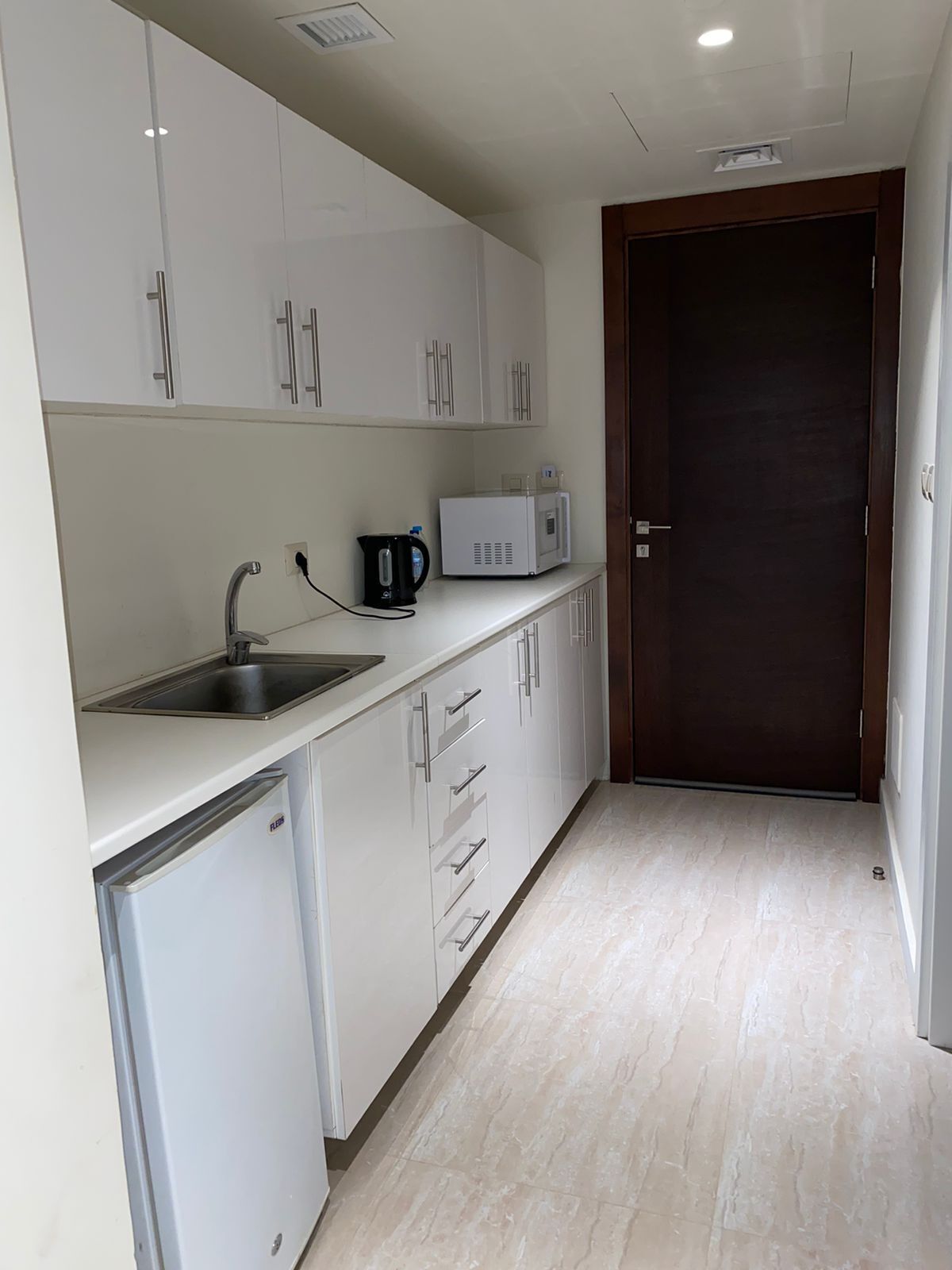 A modern kitchen with white cabinets, a built-in sink, a kettle, a microwave, and a refrigerator.