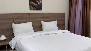 A neatly made bed with white linens, a wooden headboard, a bedside table with a lamp, and a painting on the wall.