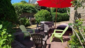 En udendørs terrasse med Adirondack-stole, et bord og en rød parasol.