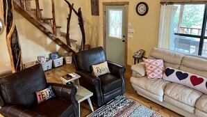 Ein gemütliches Wohnzimmer mit einer Holztreppe, Ledersofas, einem Couchtisch und einem großen Fenster mit Blick.