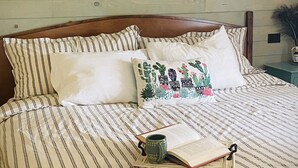 Ein Bett mit gestreifter Bettwäsche, ein Kissen mit floralem Muster, ein Buch und eine Tasse.