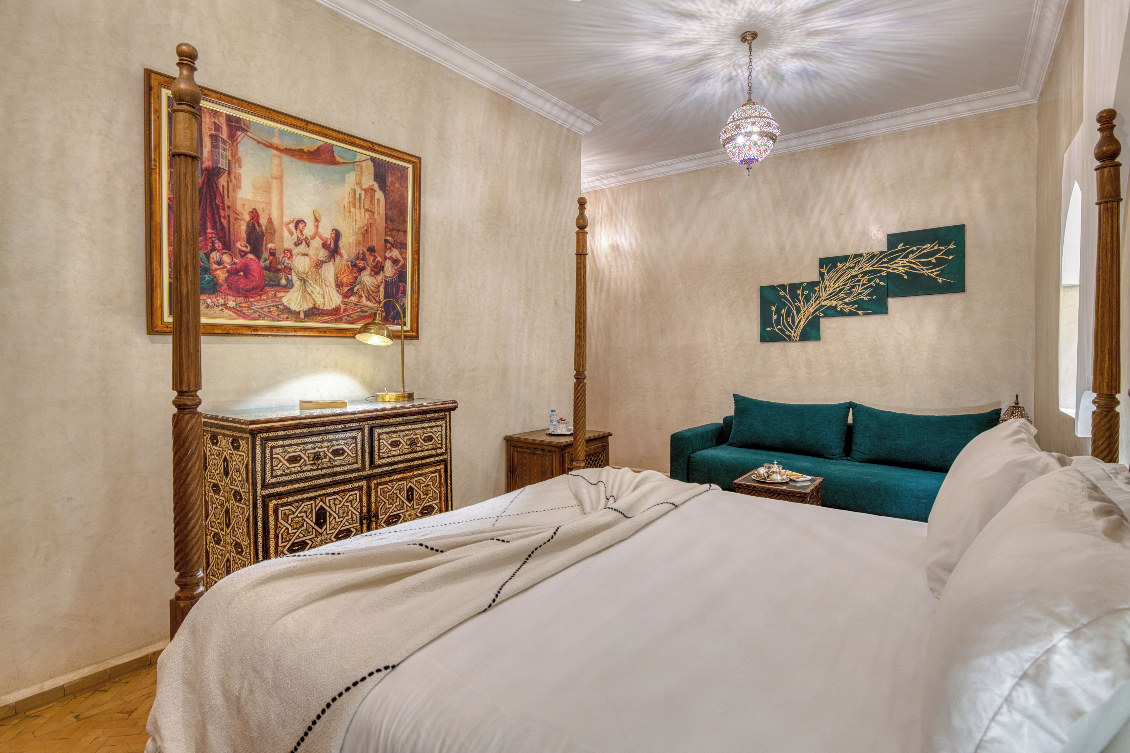 A bedroom with a large bed, a wooden dresser, a painting on the wall, and a chandelier.