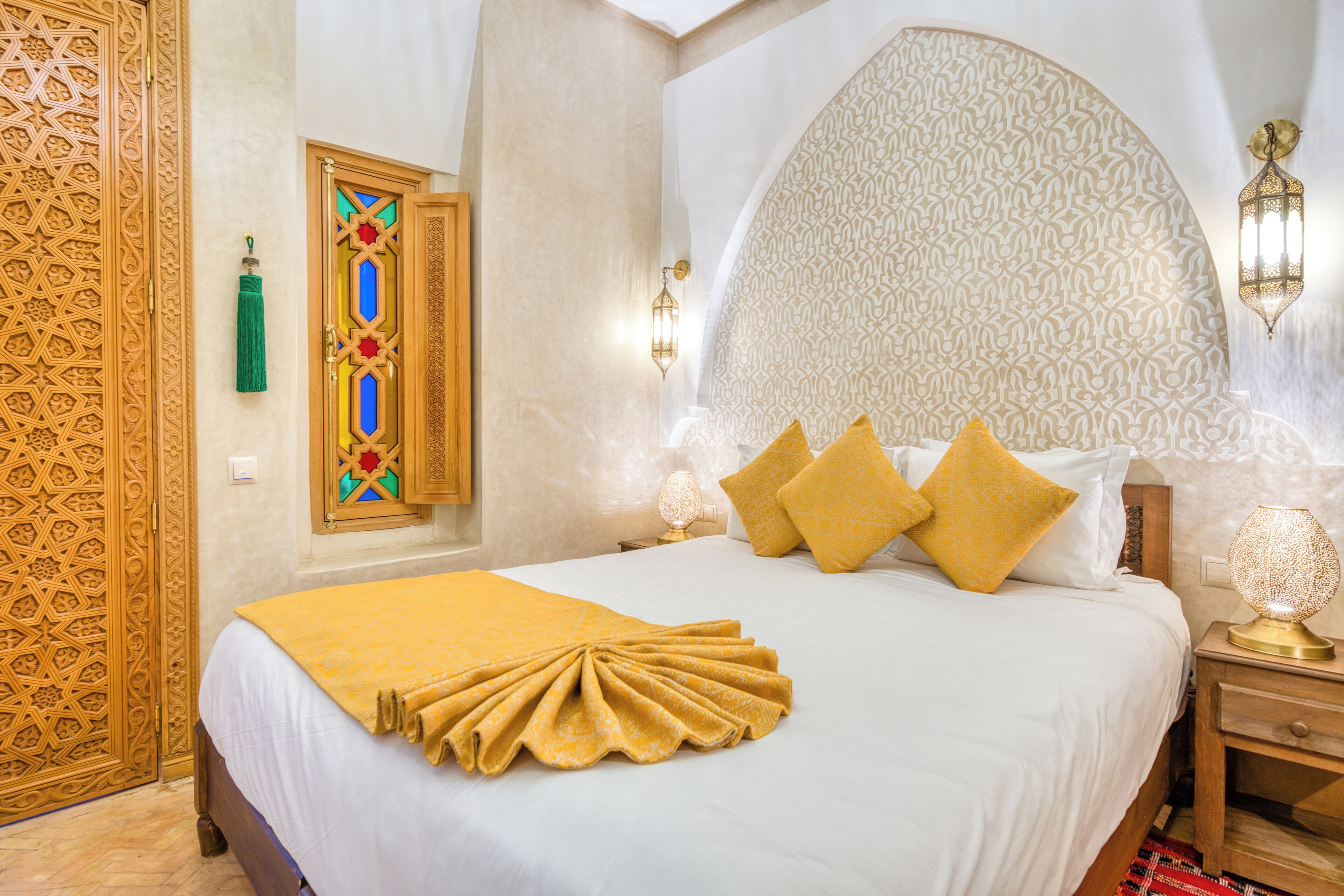 Une chambre d’hôtel avec un grand lit, des motifs décoratifs sur les murs et une frange verte suspendue à la porte.