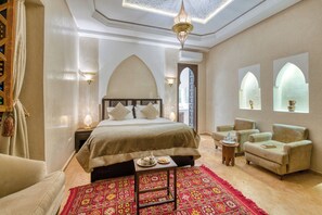 Une chambre spacieuse avec un grand lit, deux fauteuils, une petite table avec un plateau et un tapis décoratif.