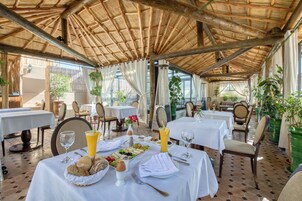 Un área de comedor al aire libre con mesas preparadas para el desayuno, mostrando pan, fruta y bebidas.