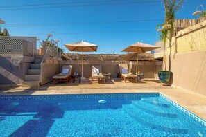 Une piscine entourée d’une clôture en bambou, agrémentée de chaises longues et de parasols, et à laquelle on accède par des marches menant à une terrasse.