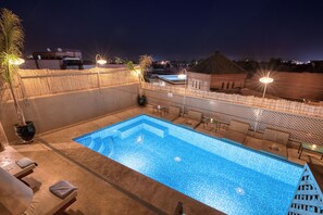 Uma piscina no terraço com um recurso de água azul cristalina, cercada por espreguiçadeiras e um portão decorativo.