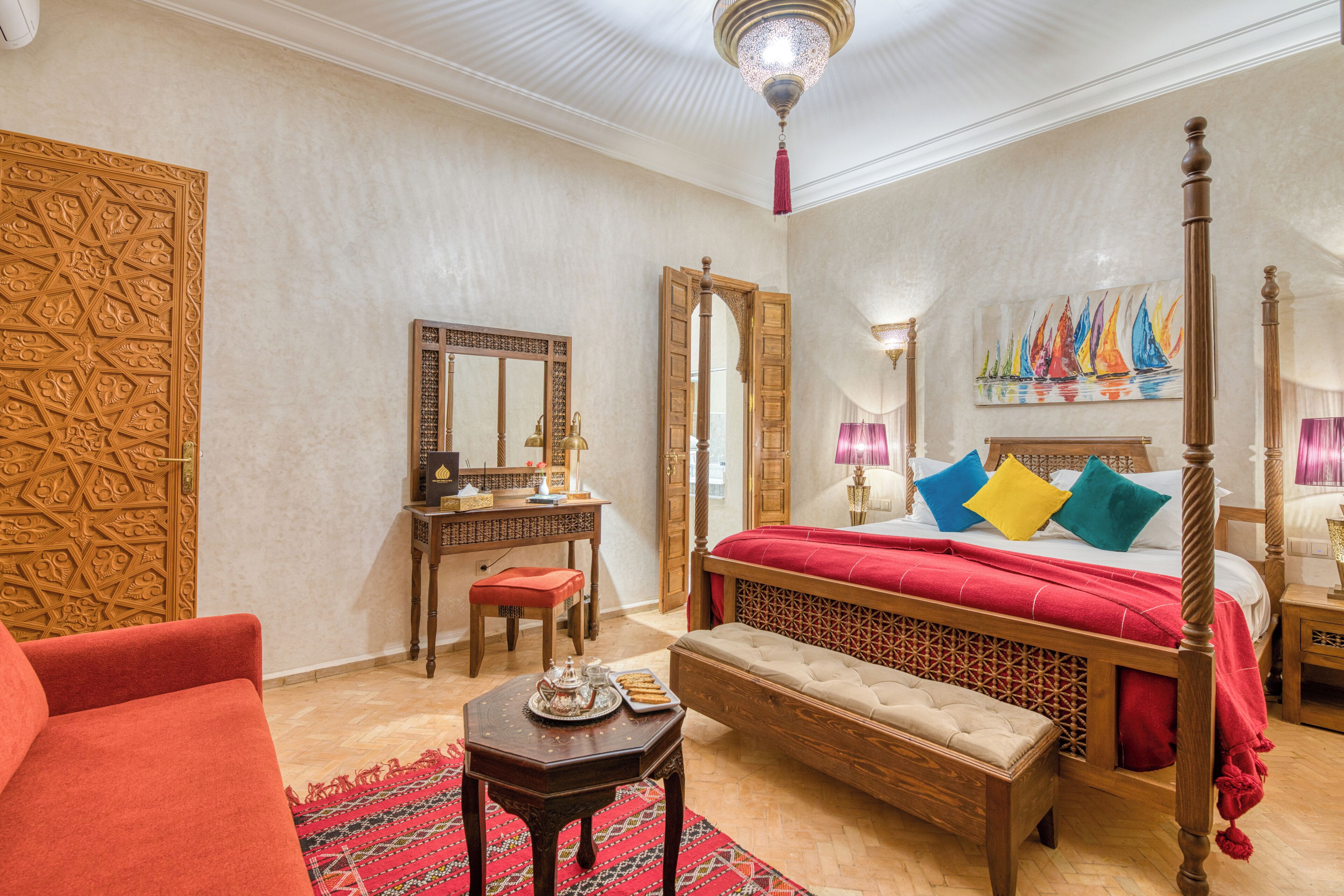 A traditional room with a four-poster bed, a wooden desk, a red armchair, and a patterned rug.